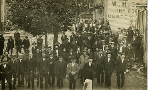 Sepia photo of a group of men standing on Main Street. A building with 