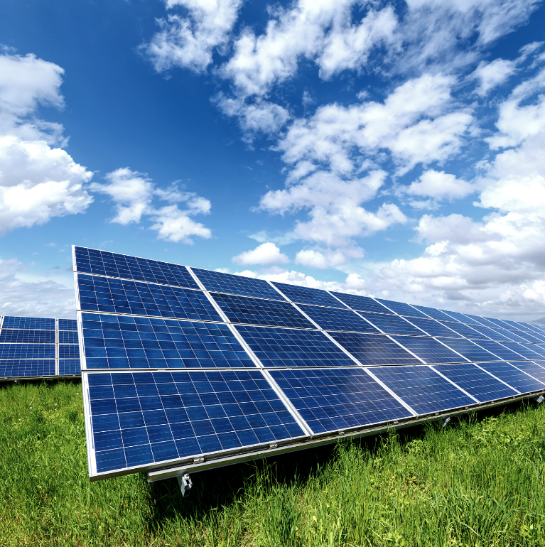 Image of solar panels on green grass with a blue sky with some clouds above. 